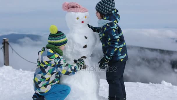 Двоє дітей, брати-хлопчики, будують сніговика, розважаються — стокове відео