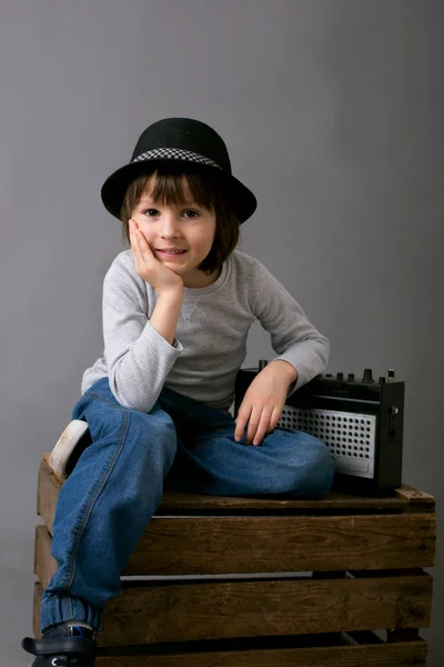 Симпатичный мальчик в черной шляпе, сидит на деревянном подносе, держит радио — стоковое фото