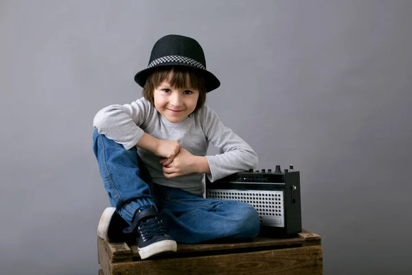 Netter Junge mit schwarzem Hut, sitzt auf einem Holztablett und hält ein Radio in der Hand — Stockfoto