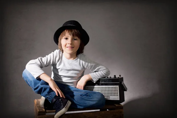 Netter Junge mit schwarzem Hut, sitzt auf einem Holztablett und hält ein Radio in der Hand — Stockfoto