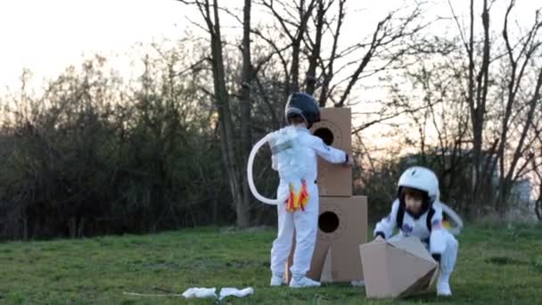 Twee schattige kinderen, broertjes, spelend in het park bij zonsondergang, gekleed als astronauten, denkend dat ze op de maan vliegen. — Stockvideo