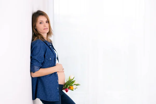 Jovem grávida, segurando flores de tulipa, apoiando-se em uma parede — Fotografia de Stock