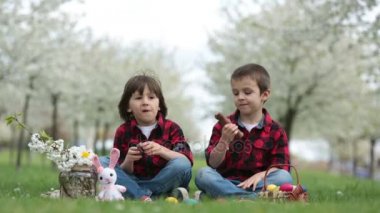 İki çocuk, erkek kardeşler, çikolata tavşanlar yemek ve parkta güzel bahar Çiçek Bahçe having oyunculuk ile Paskalya yumurtaları