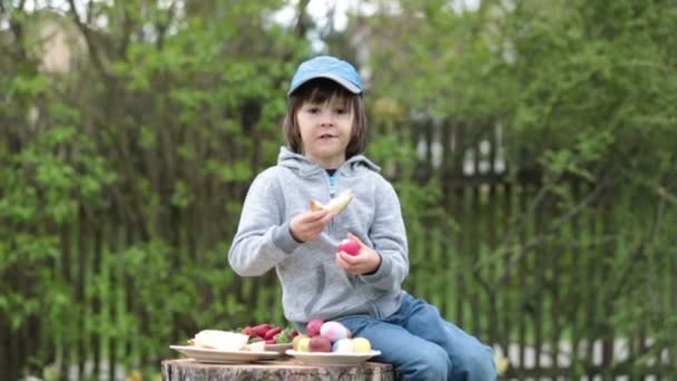 Niedliches Kind, Spaß mit Ostereiern im Park, süßes Brot essen — Stockvideo