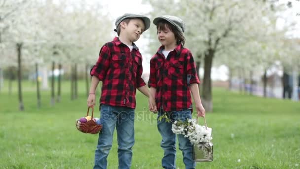 Zwei Kinder, junge Brüder, Spaß mit Ostereiern im Park, schöner frühlingsblühender Garten — Stockvideo