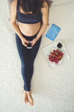 Genç hamile kadın, smartphone, kitap, kahve ile yatakta yalan