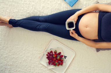Genç hamile kadın, smartphone, kitap, kahve ile yatakta yalan
