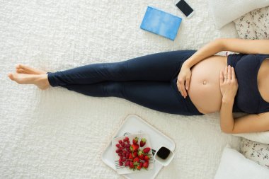 Genç hamile kadın, smartphone, kitap, kahve ile yatakta yalan