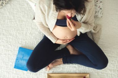 Genç hamile kadın, smartphone, kitap, kahve ile yatakta yalan
