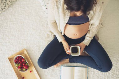 Genç hamile kadın, smartphone, kitap, kahve ile yatakta yalan