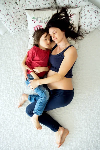 Беременная молодая мать и ее ребенок, мальчик, лежат в постели — стоковое фото