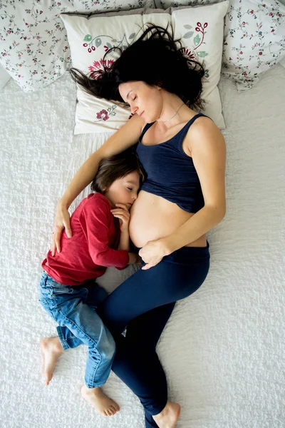 Bela grávida jovem mãe e seu filho, menino, deitado na cama — Fotografia de Stock