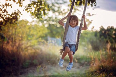 Sevimli çocuk, çocuk, bahçedeki bir salıncak üzerinde eğleniyor 