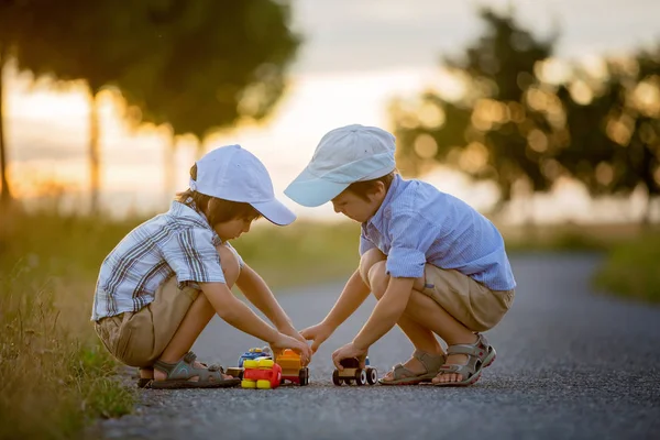 Due bambini, fratelli maschi, si divertono all'aperto con macchine giocattolo — Foto Stock