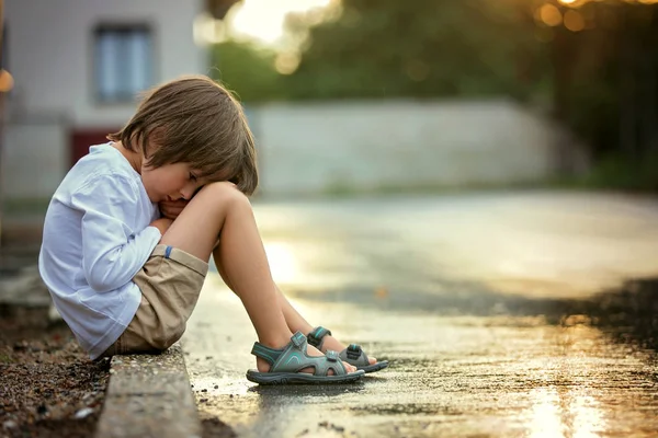 Triste niño, sentado en la calle bajo la lluvia, abrazando su t —  Fotos de Stock