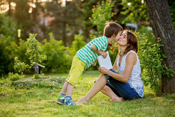 Νεαρή όμορφη μητέρα, κάθεται σε ένα κήπο, μικρό αγόρι, ο γιος της — Φωτογραφία Αρχείου