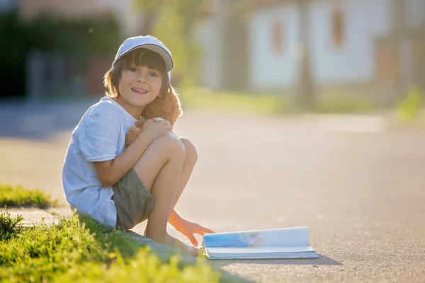Beautiful kid boy, reading a book on the street, sitting down wi — Stock Photo, Image