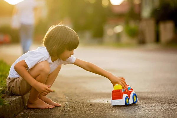 Lindo niño dulce, niño, jugando con juguetes de coche en la calle en vi —  Fotos de Stock