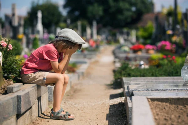 Üzgün bir mezarlığındaki mezar taşındaki oturan üzgün küçük çocuk, — Stok fotoğraf