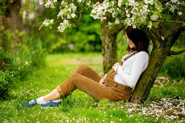 Молодая беременная женщина, сидящая в цветущем саду — стоковое фото