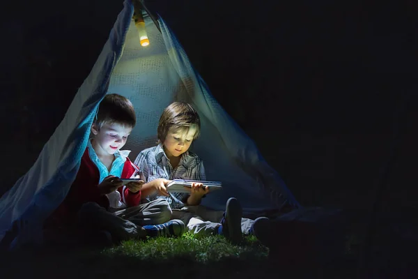 Carino fratellini, giocando su tablet e telefono di notte i — Foto Stock