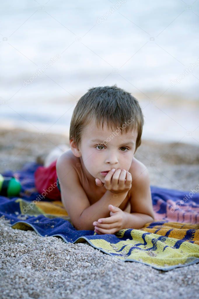 Portrait of cute child, boy, contemplating the beach, lying down