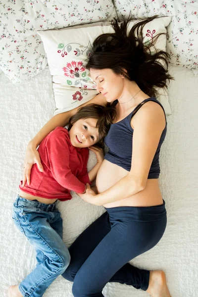 Hermosa madre joven embarazada y su hijo, niño, acostado en la cama — Foto de Stock