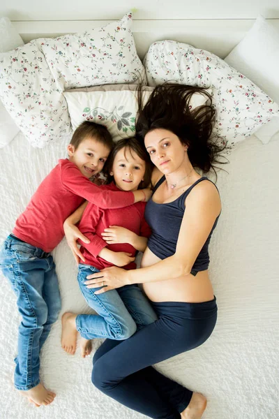 Όμορφη έγκυος νεαρή μητέρα και το παιδί της, αγόρι, ξαπλωμένη στο κρεβάτι — Φωτογραφία Αρχείου