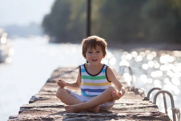 Schattig kind, jongen, zittend op de kust van een meer, avond portret — Stockfoto