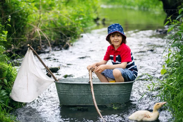 Lindo niño, niño, jugando con el barco y patos en un pequeño río — Foto de Stock