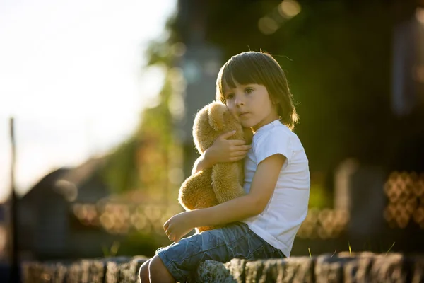 Dulce niño, jugando con el oso de peluche en un pequeño camino rural en los soles — Foto de Stock