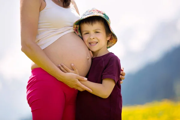 Jovem mulher grávida e seu filho em um campo de dente de leão em Alpes — Fotografia de Stock