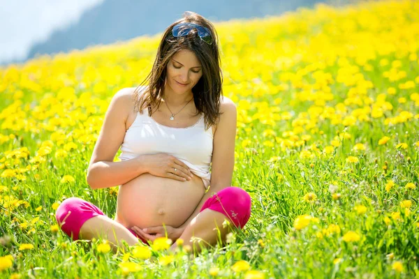Mujer embarazada joven, sentada en un campo de diente de león —  Fotos de Stock