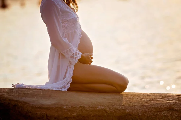 Hermosa mujer embarazada, sentado en la orilla de la playa en s —  Fotos de Stock