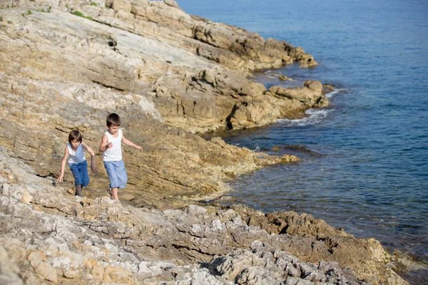 Dos niños, chicos, corriendo sobre rocas en la orilla del mar — Foto de Stock