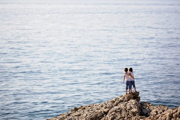 Δύο παιδιά, στέκεται πάνω σε βράχια στην ακτή της θάλασσας — Φωτογραφία Αρχείου