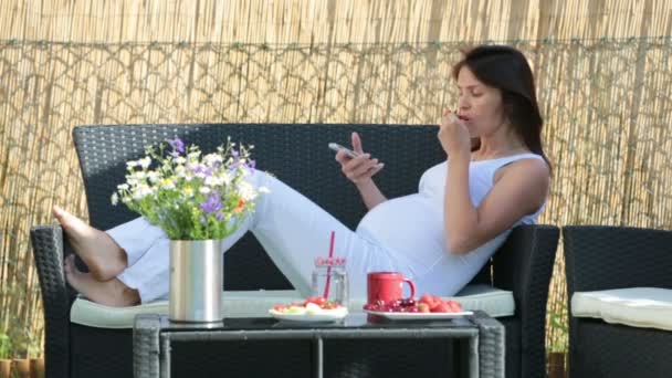 Giovane donna incinta, con colazione sana, caffè, frutta e lettura di un libro in un giardino sul retro — Video Stock