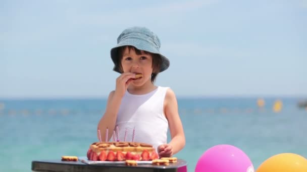 Doux petit enfant, garçon, célébrant son sixième anniversaire sur la plage, gâteau, ballons, bougies, biscuits. Concept de bonheur de l'enfance — Video