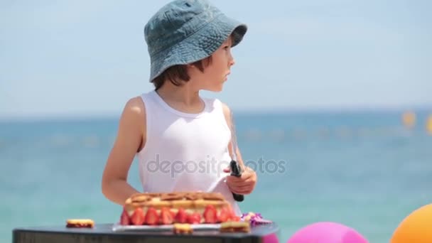 Criança doce, menino, comemorando seu sexto aniversário na praia, bolo, balões, velas, biscoitos. Conceito de felicidade infantil — Vídeo de Stock