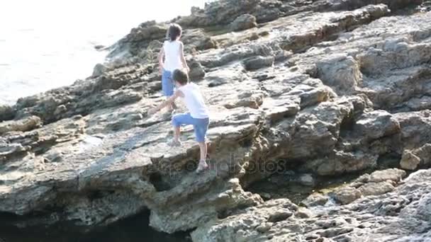 Két gyermek, fiúk, futás a sziklák, a tenger partján, szórakozás — Stock videók