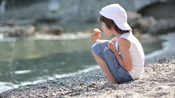 Lindo niño en la playa, comiendo pan y jugando con guijarros — Vídeo de stock