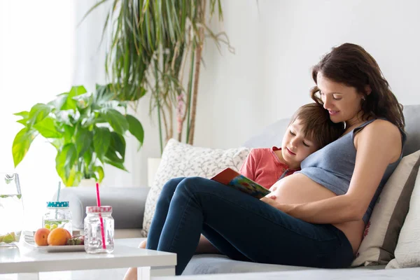 Jonge zwangere vrouw, het lezen van een boek thuis met haar jongen — Stockfoto