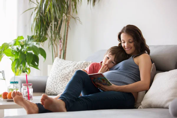Молодая беременная женщина, читает книгу дома своему сыну — стоковое фото