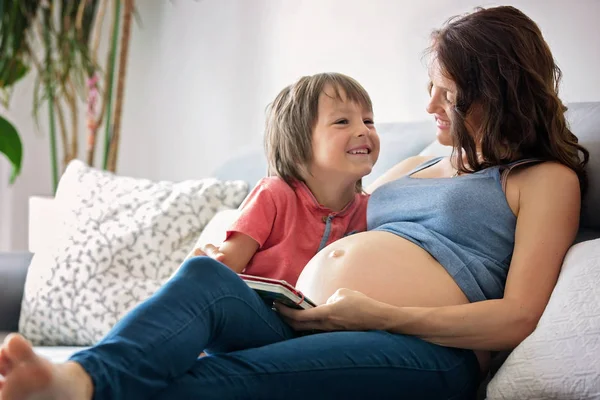 Νεαρή έγκυος γυναίκα, διαβάζοντας ένα βιβλίο στο σπίτι με το αγόρι της — Φωτογραφία Αρχείου