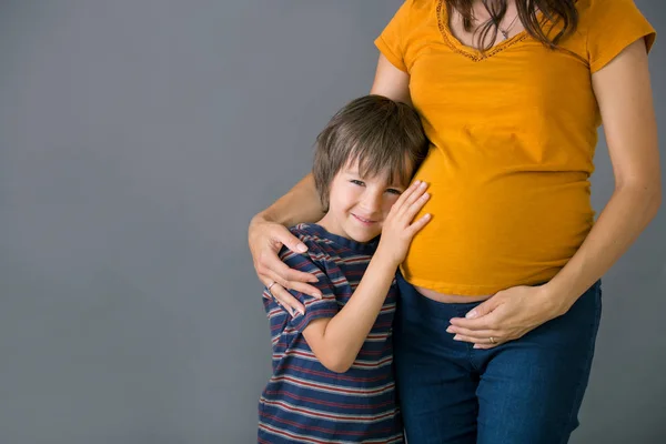 Маленький ребенок, мальчик, обнимающий беременную мать дома, изолированный — стоковое фото