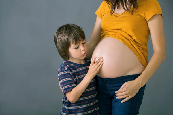 Niño pequeño, niño, abrazando a su madre embarazada en casa, aislado —  Fotos de Stock