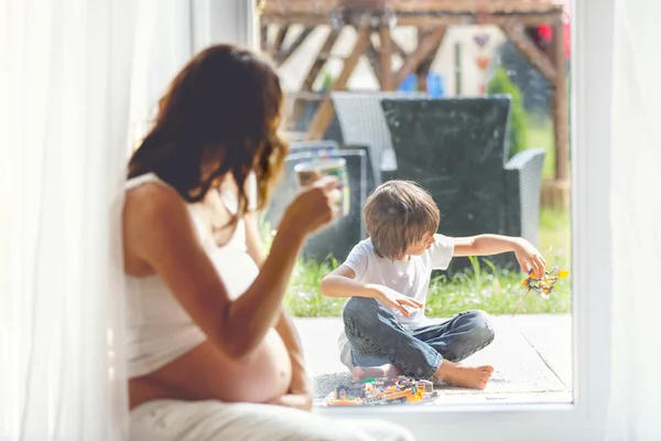 Giovane donna incinta, seduta al coperto, guardando il suo bambino attraverso — Foto Stock