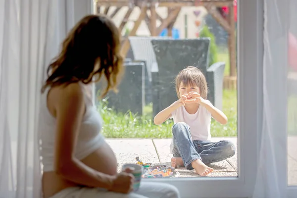 Giovane donna incinta, seduta al coperto, guardando il suo bambino attraverso — Foto Stock