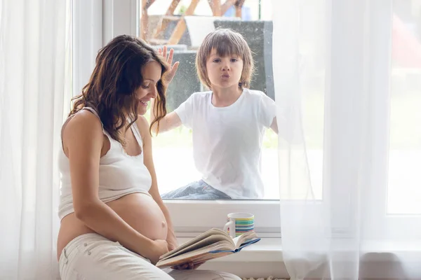 Giovane donna incinta, seduta al coperto, guardando il suo bambino attraverso — Foto Stock