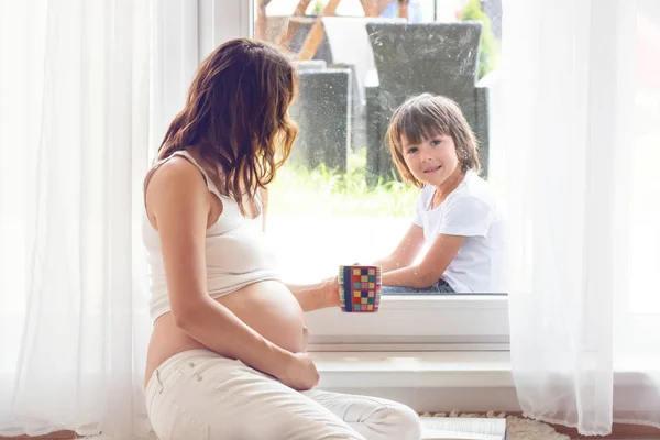 Giovane donna incinta, seduta al coperto, guardando il suo bambino attraverso — Foto Stock